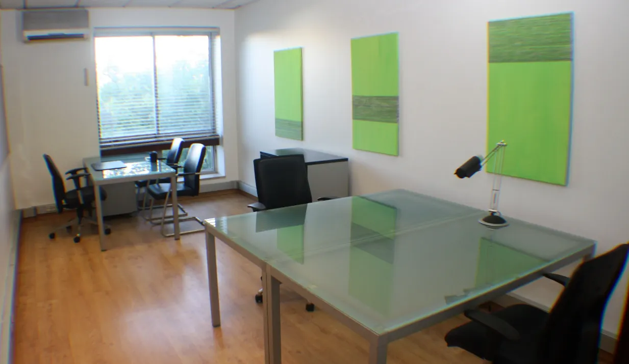 Escritório com quadros verdes, mesa de vidro e janela